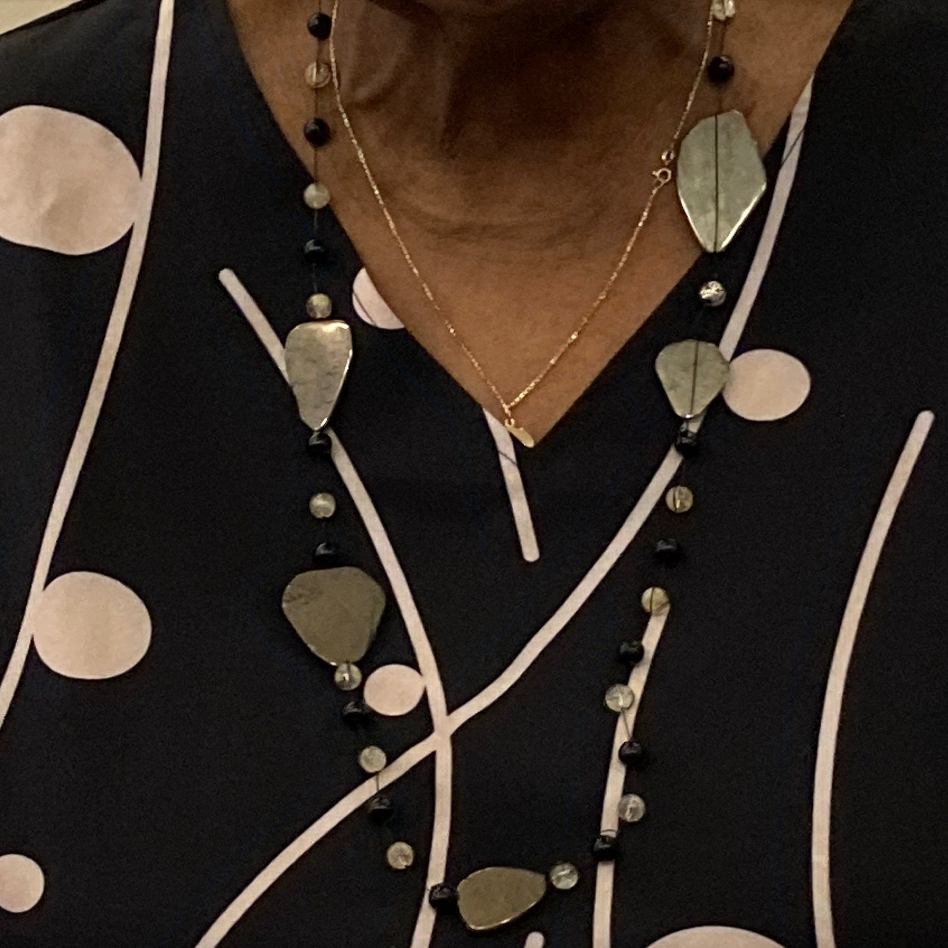 Peaceful Prosperity is a closeup of a woman wearing a hand knotted necklace with pyrite slabs of 20-30mm necklace with an alternating pattern of citrine beads and tourmaline beads 6mm. Each pyrite slab separates a section of beads following a pattern of 3-6-9 twice.  