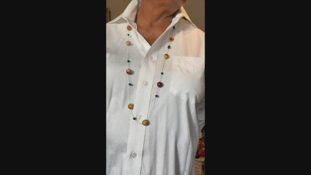 16mm mookaite beads in yellow and burgundy colours, hand knotted in groups of three with 4mm black agate beads on a white shirt. 